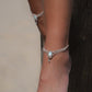 Duo de Bracelets de cheville bohème, ambiance plage et été sur les îles. Bijoux de pieds assortis. Micro macramé en fil de coton couleur lin beige avec une pierre de larimar bleu ciel accompagné d'une perle goutte argenté. Système de réglage à coulisse à l'arrière. Bijou porté sur une cheville dénudée à la peau caramel dans un univers sirène, marin avec bois flotté et sable fin.