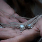 Duo de Bracelets de cheville bohème, ambiance plage et été sur les îles. Bijoux de pieds assortis. Micro macramé en fil de coton couleur lin beige avec une pierre de larimar bleu ciel accompagné d'une perle goutte argenté. Système de réglage à coulisse à l'arrière. Bijoux posé sur 2 mains dans un univers féérique bohème dans un jardin. Modèle avec Dreadlocks brunes, peau caramel et habits assorti au bijou de couleur lin naturel beige gris