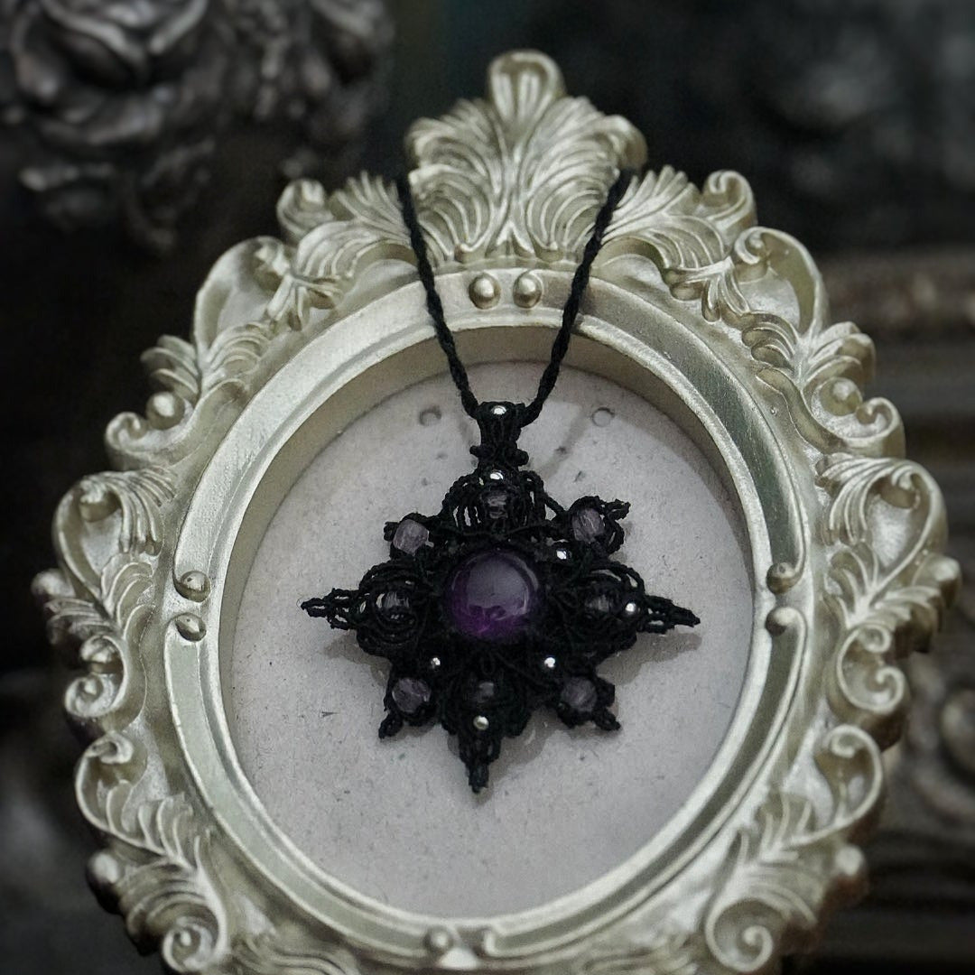 Bijou elfique sombre en micro macramé noir, pendentif étoile lumineux photographié sur fond gothique romantique. Coton et Astrance