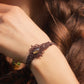 Bracelet réglable en micro macramé. Bijou féminin composé d'une citrine jaune ovale translucide au centre, entourée de 6 perles en grenat rouge à facettes de 3 mm puis de 3 perles dorées de 2 mm. Fil de coton de 0.4 mm tissé en micro macramé avec de motifs en reliefs type nœuds celtiques et motifs arabesques  féériques et elfiques. Bijou large ambiance et style bohème hippie, fairycore et wicca.

Photo du bijou porté sur un poignet de femme  la peau claire, cheveux marron, prise de vue de face avec le modèl