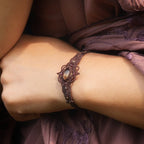 Bracelet large elfique en micro macramé brun, orné d’une citrine jaune pâle et de perles de grenat rouge rosé. Bijou bohème et artisanal réglable, porté au poignet d’une femme à la peau claire.
